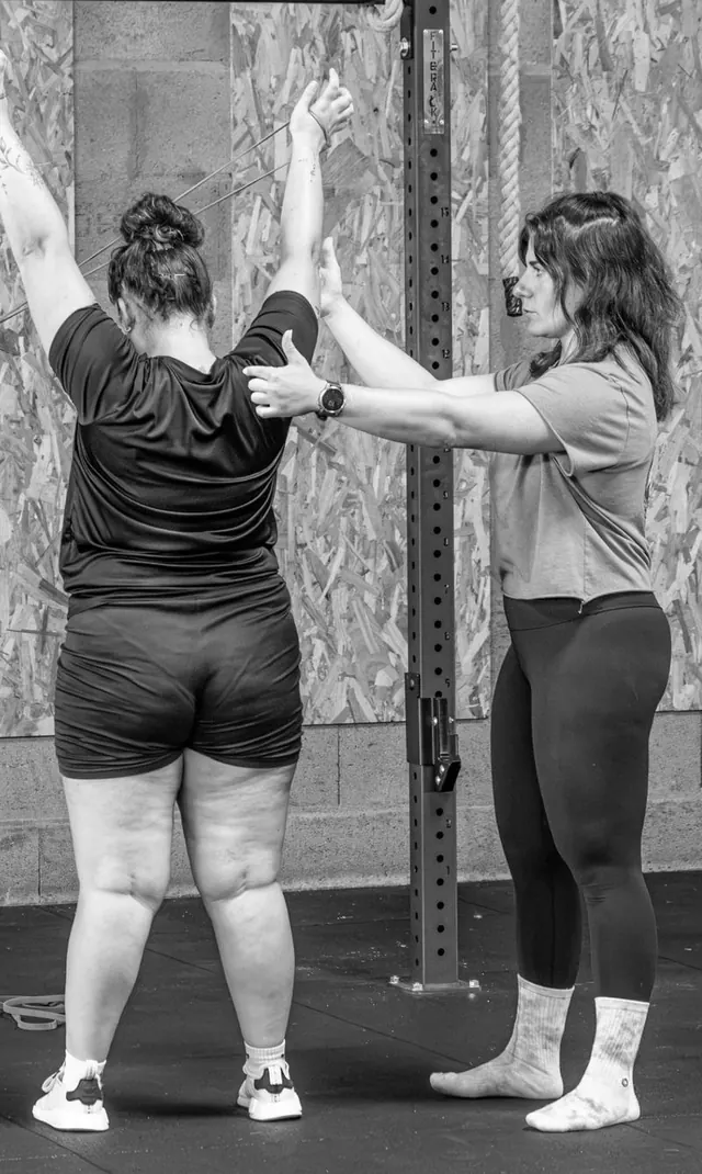 Coach corrigeant la posture d'une adhérente pendant un exercice à l'élastique